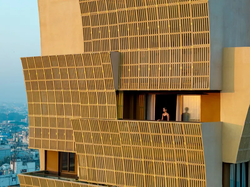 Cantilevered terrace with vertical brick screen and a figure standing at the railing at sunset