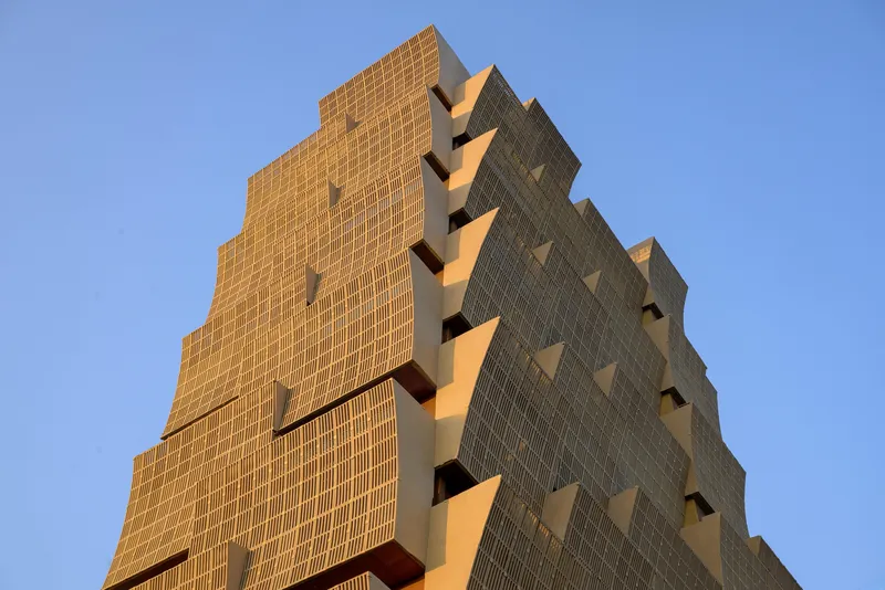 Upward view of the stepped tower facade with ribbed brick and deep recessed balconies against a clear sky