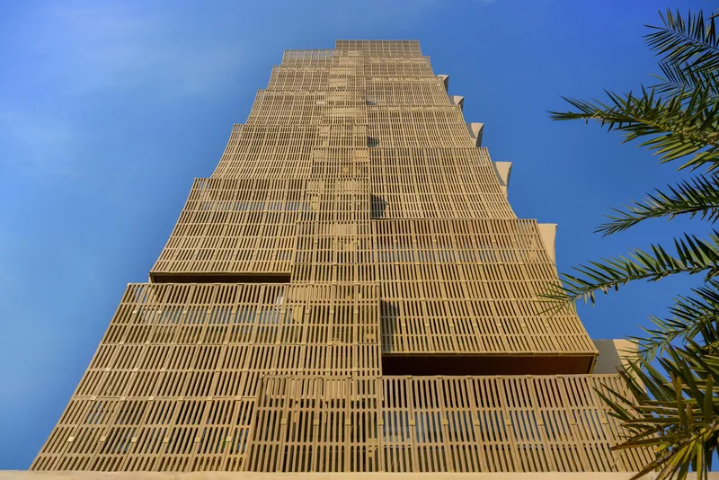 Full elevation of the stepped tower with ribbed brick facade framed by palm fronds in the foreground