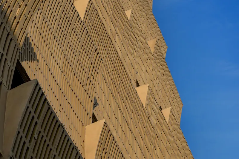 Upward view of perforated facade with diagonal pattern of openings against a clear blue sky