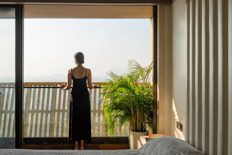 Bedroom view with a figure on the balcony overlooking hazy landscape through vertical louvers