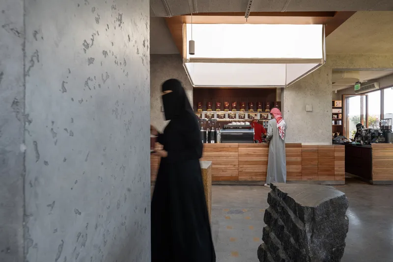 Interior with concrete columns and square skylight above coffee bar as a person walks past stone sculpture