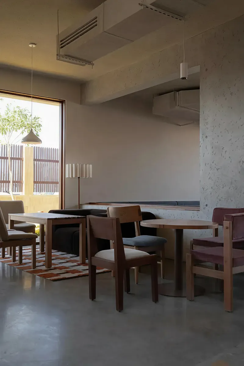 Seating area with timber tables and chairs on patterned rug beneath window overlooking bamboo screening