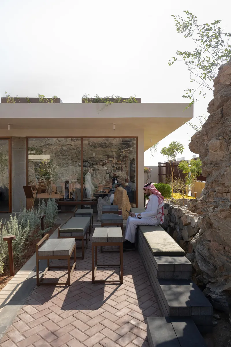 Outdoor terrace with herringbone brick paving and glazed doors opening to an interior with figures seated inside