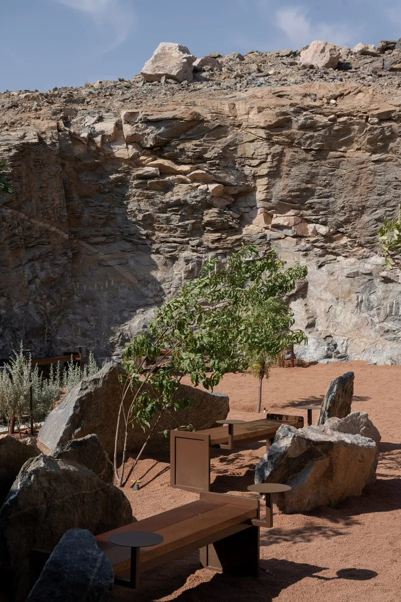 Reddish sand terrace with timber benches and planters nestled against weathered rock formations
