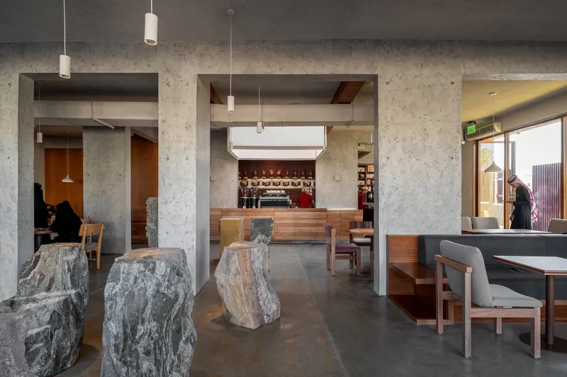 Dining area with exposed concrete columns, raw stone table bases, and pendant lights suspended from the dark ceiling