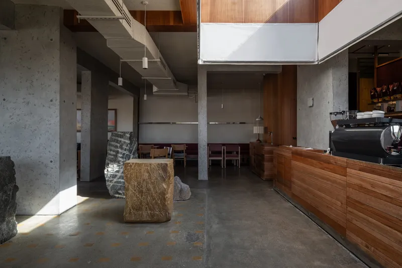 Interior space with a central skylight, concrete columns, timber millwork counter, and large boulder fragments scattered across the floor