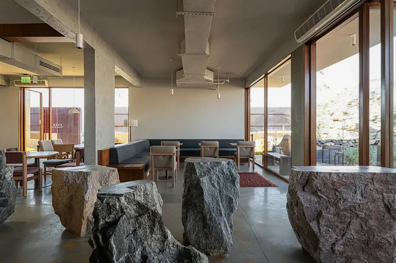 Seating area framed by glazed openings to outdoor terraces, with rough stone boulders emerging from the polished concrete floor
