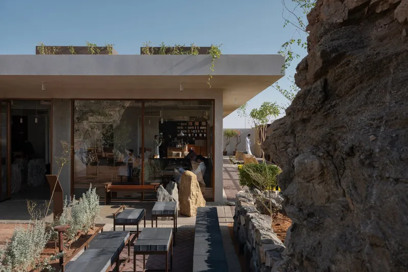 Covered patio nestled against a natural rock outcrop with planted roof edges and dark timber loungers in afternoon light