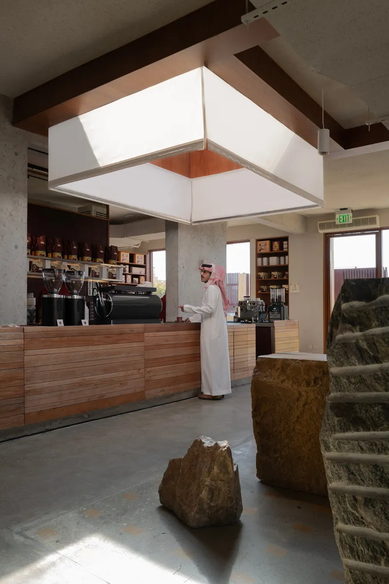 Coffee bar with horizontal wood cladding and large square skylight fixture suspended from exposed timber beams