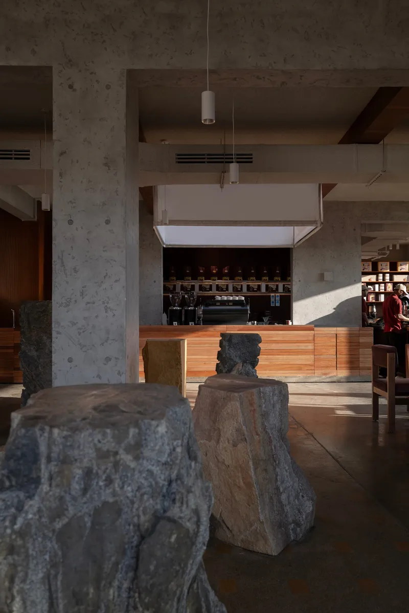 Raw stone blocks arranged on polished concrete floor beneath suspended square light fixture and coffee counter