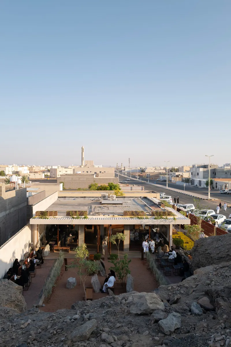 Elevated view of a roofed structure with planted rooftop terraces overlooking a surrounding neighborhood at dusk