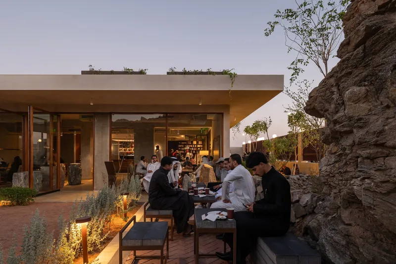 Evening terrace scene with diners seated along tables beside rock wall and illuminated planting beds