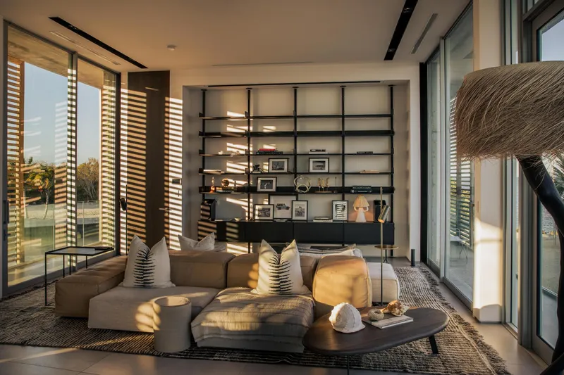 Living room with timber louvered screens filtering afternoon light onto shelving and seating below