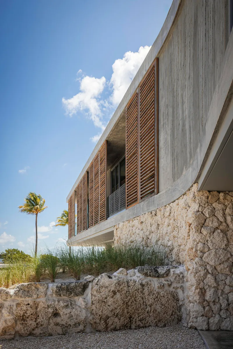 Concrete volume with horizontal timber louvres set above terraced coral stone walls with palms