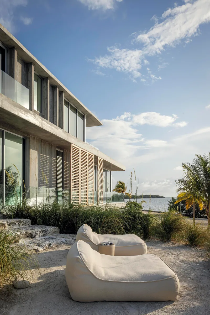 Outdoor terrace with curved white loungers and planted grasses facing the water at dusk