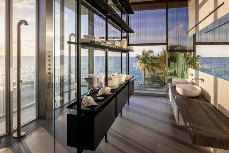 Glass-enclosed bathroom with freestanding shower and double vanity opening to an ocean view terrace