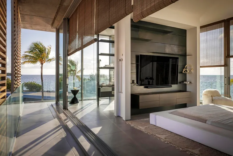 Bedroom with integrated media wall and sliding glass doors opening to poolside terrace with palm trees