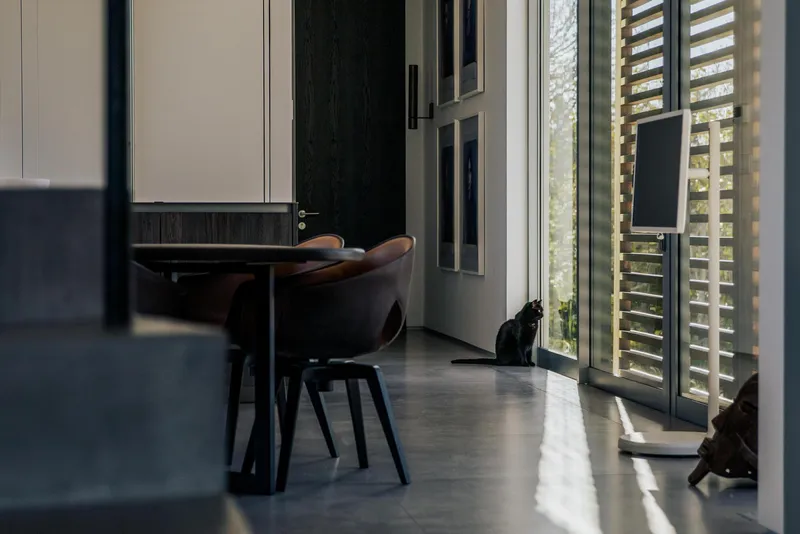 Dining area with round table and timber louvered screens filtering afternoon light onto polished floor