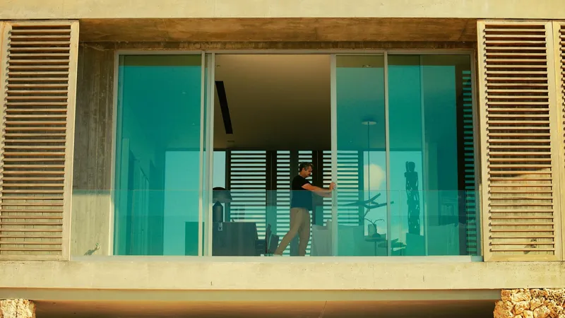 Exterior balcony with glass sliding doors, timber louvered screens, and a person seated inside in afternoon light