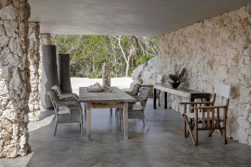 Covered terrace with textured coral stone walls, polished concrete floor, and dining furniture beneath a smooth ceiling