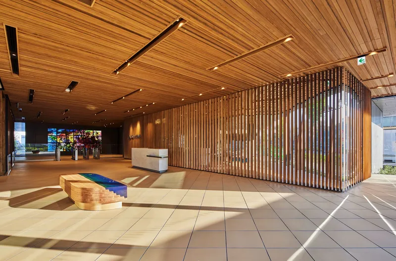 Entrance lobby showing timber slatted wall and ceiling with carved wooden bench and sunlight through glazing