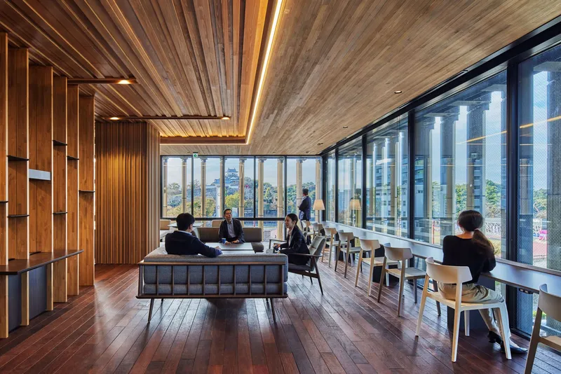 Upper floor lounge with timber ceiling, floor-to-ceiling glazing, and occupied seating areas overlooking the surroundings