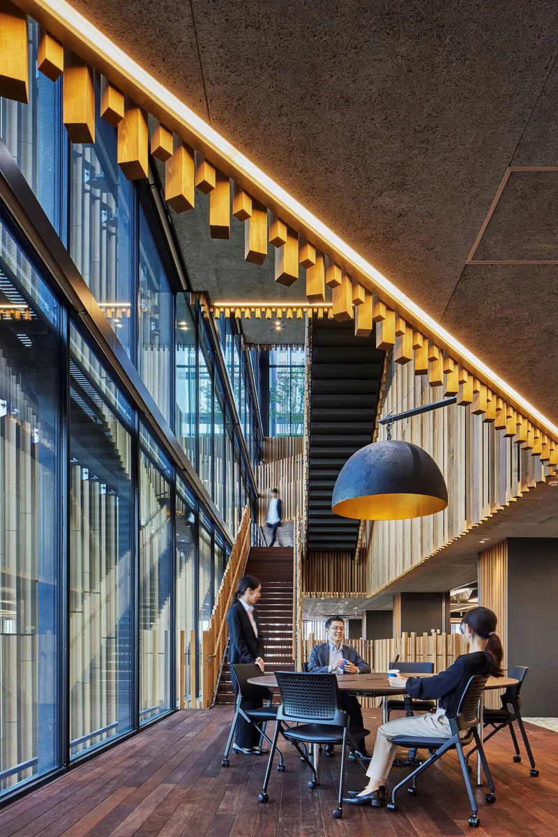 Meeting area beneath suspended pendant light and yellow acoustic baffles with timber staircase and glazed wall beyond