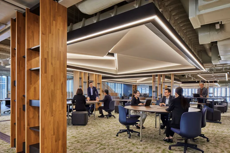 Open office workspace with timber columns and suspended geometric light fixture over collaborative tables