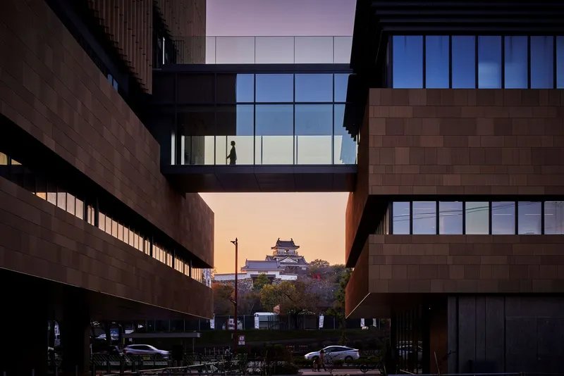 Courtyard view framing temple structure through gap between timber-clad volumes at dusk
