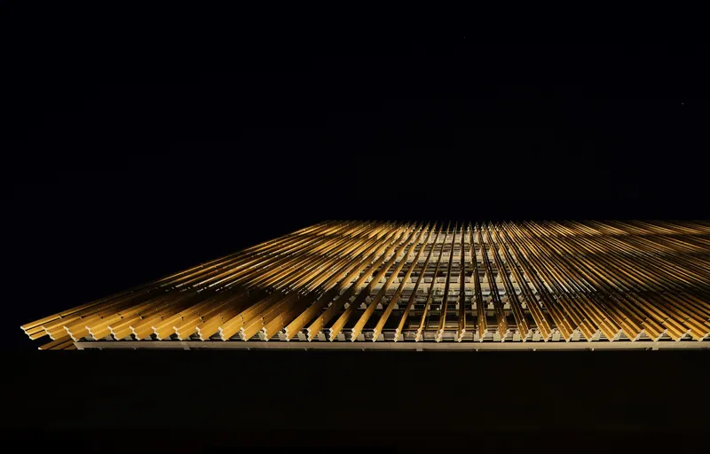 Upward night view of illuminated timber louver facade receding into darkness