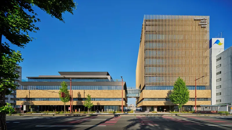 Street view showing the low-rise horizontal volumes and vertical timber-screened tower under a clear blue sky