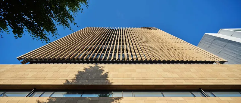 Upward view of the cantilevered timber louver canopy casting shadows on the pale stone facade below
