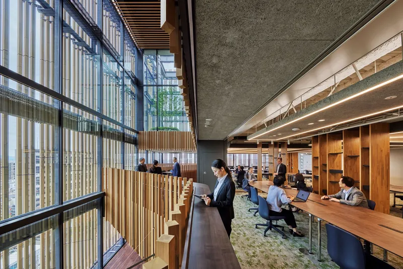 Shared workspace with timber desks beside a vertical wood slat screen and floor-to-ceiling glazing