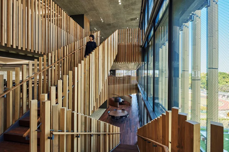 Interior view through vertical timber battens toward the glazed facade with figures on stairs and seating