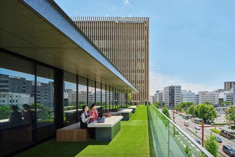 Rooftop terrace with artificial grass, bench seating, and glass balustrade overlooking the surrounding cityscape