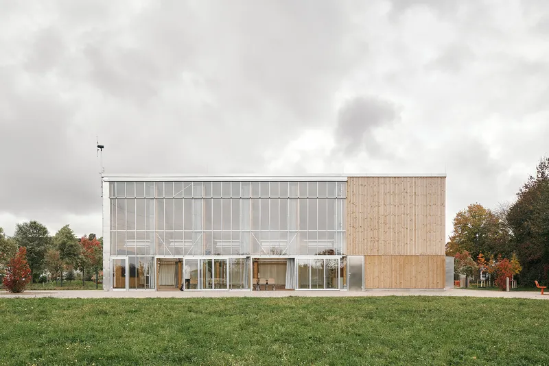 Long west elevation with the full-height greenhouse facade alongside a closed timber block