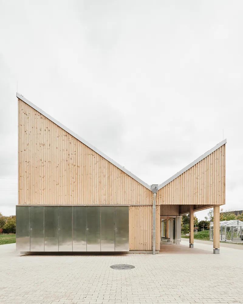 Close approach to the entrance from the brick-paved plaza, showing the folded zinc-clad base