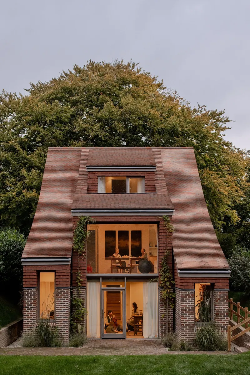 Front elevation showing stacked glazed openings and inhabitants visible inside at twilight