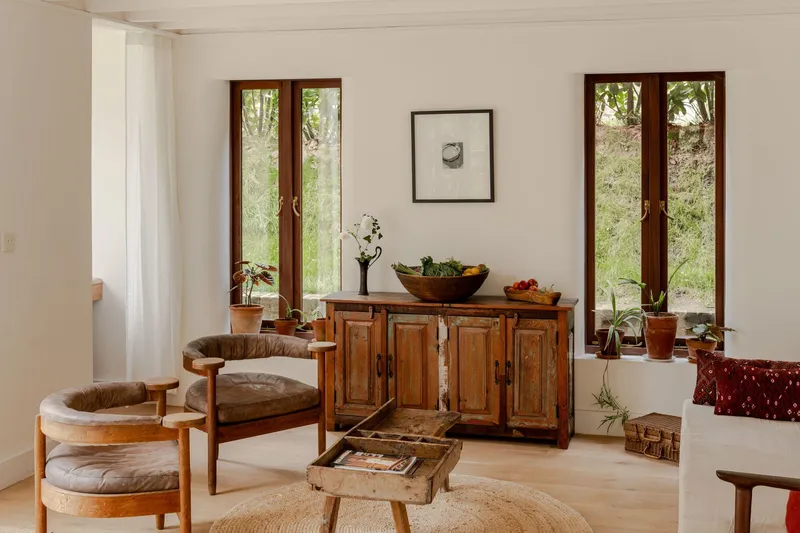 Sitting area with antique cabinet and paired timber casement doors framing views of native grasses outside