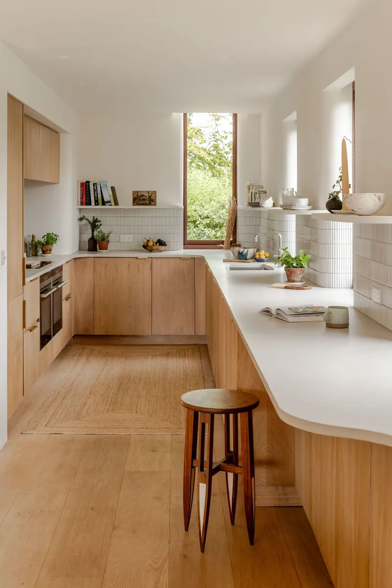 Galley kitchen with oak cabinetry and vertical window overlooking green foliage