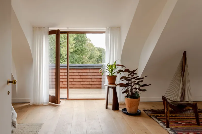 Upper floor corridor with arched ceiling leading to glazed door opening onto a timber-screened balcony