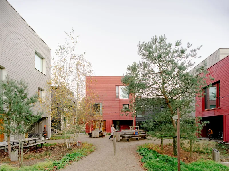 Shared courtyard path with planted beds and timber benches between red and grey clad housing blocks