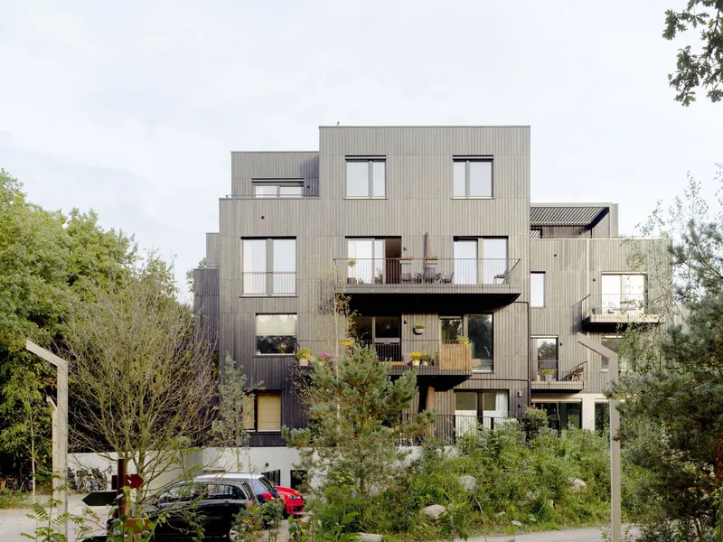 Staggered timber-clad facade with projecting balconies and square windows seen from the landscaped front