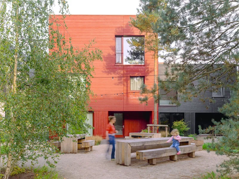 Communal courtyard with timber seating platforms and planters framed by corrugated metal facades and trees