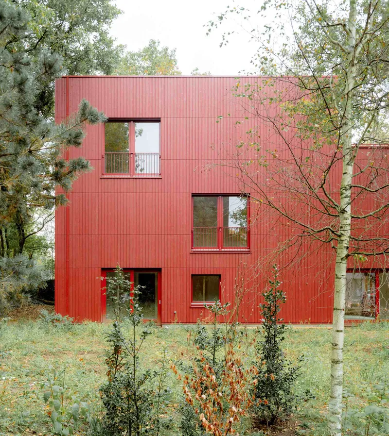 Red corrugated metal facade with offset windows set among birch trees and wild grasses in autumn