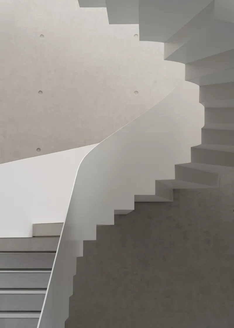 Overlapping concrete staircases with curved wall and recessed fasteners in soft daylight