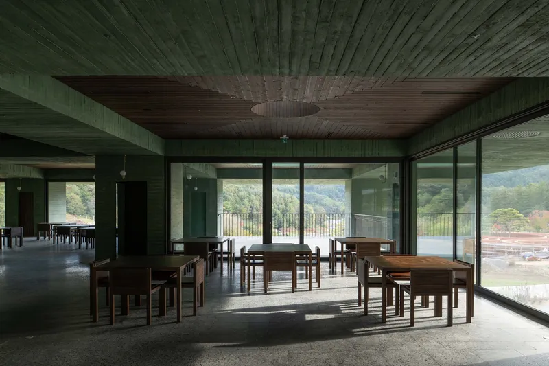Interior dining space with timber tables and chairs beneath a green wood-paneled ceiling with circular aperture