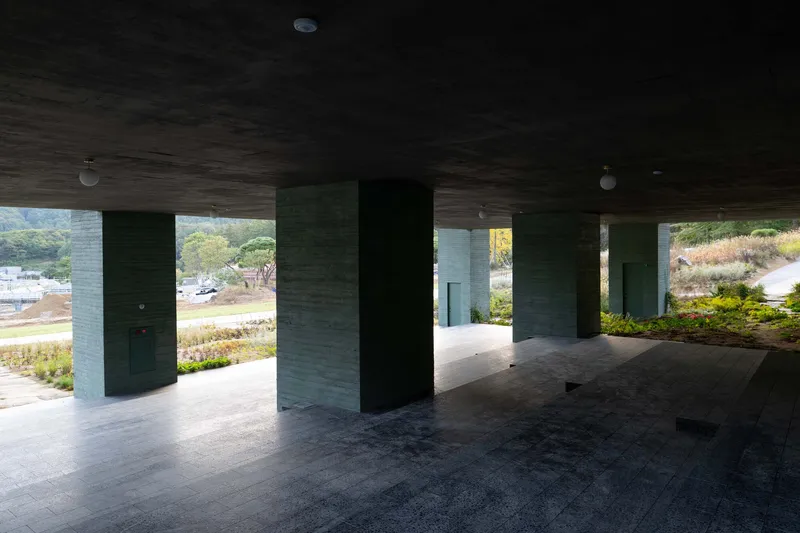 Covered ground level terrace with board-formed concrete columns framing views to landscaped beds beyond