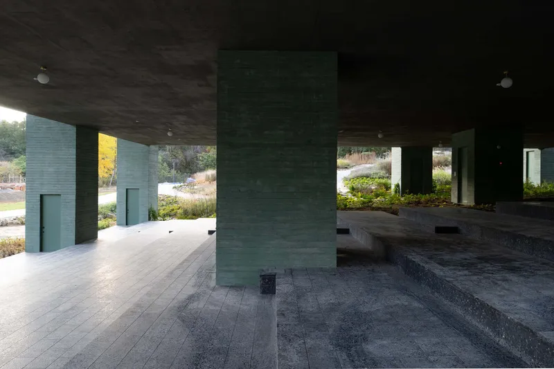 Sheltered plaza space with green concrete columns and terrazzo paving under a dark soffit